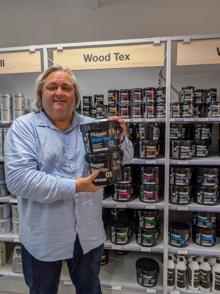 mann i blå skjorte holder frem to spann med maling inne i en fargehandel