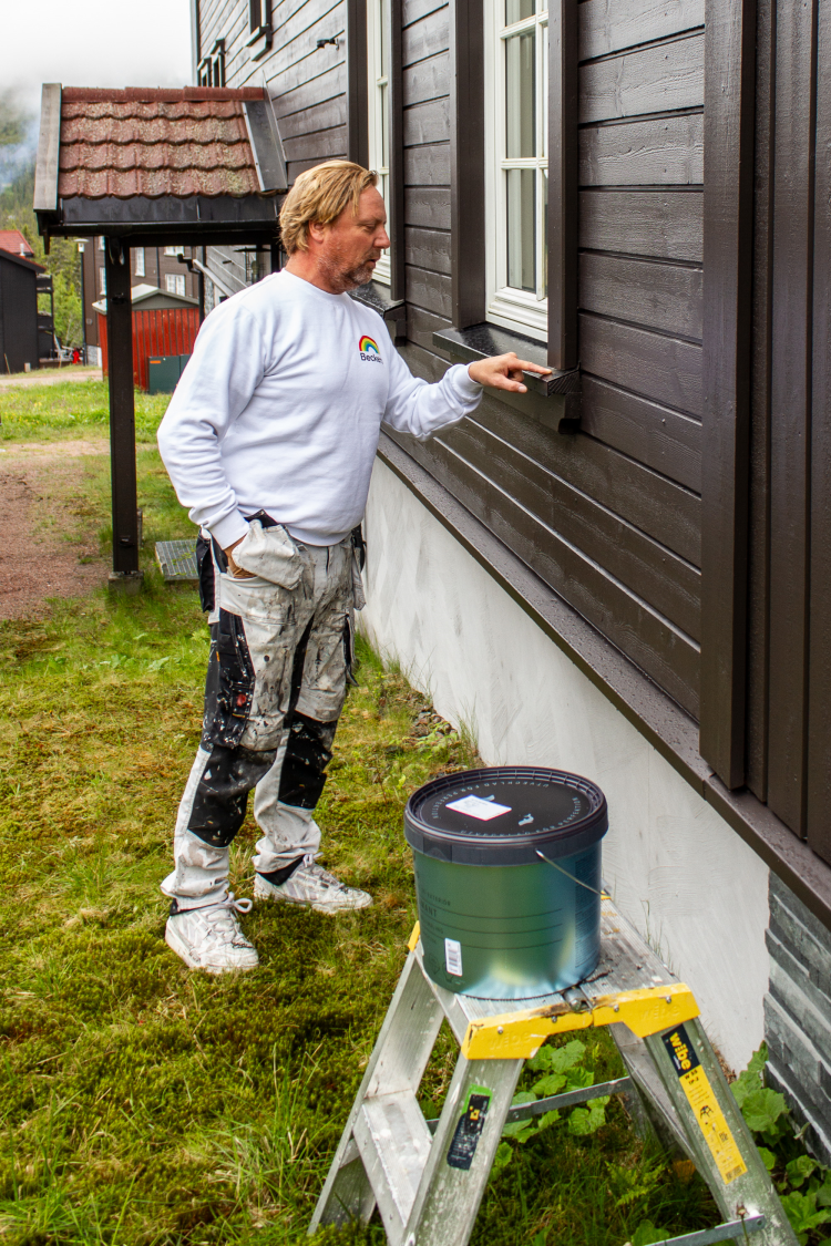maler i arbeidsklær gransker kledningen på en brun fasade