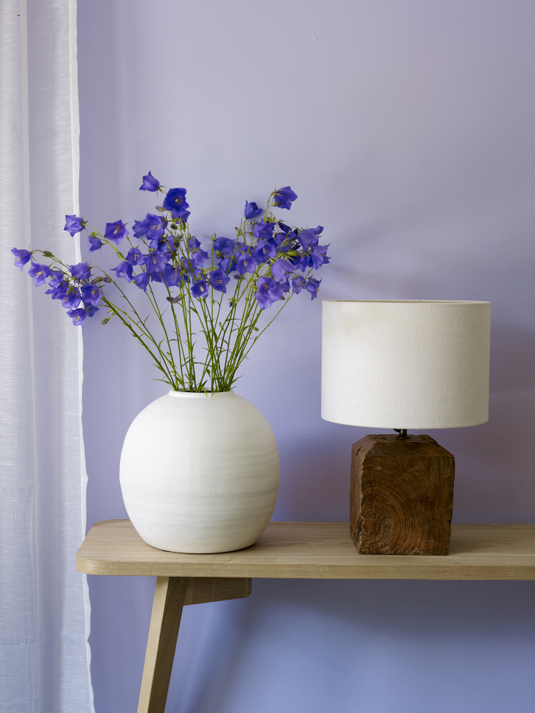 lilla blomster i hvit vase mot lilla vegg