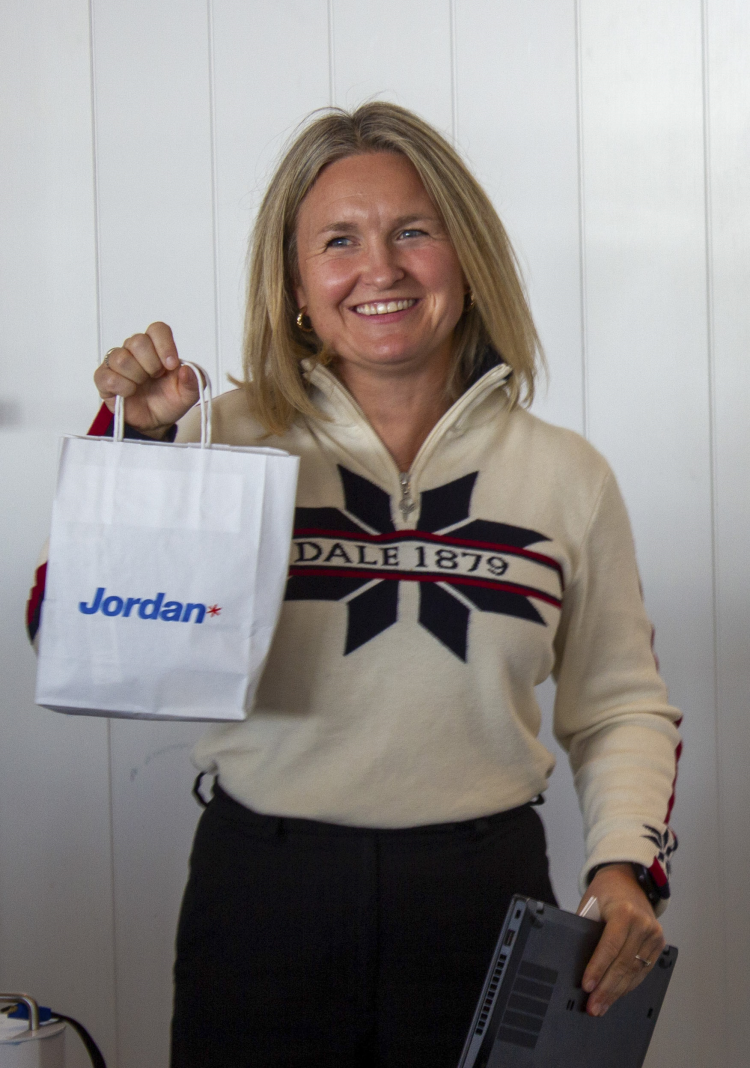 smilende dame i strikkegenser holder frem papirpose fra Jordan