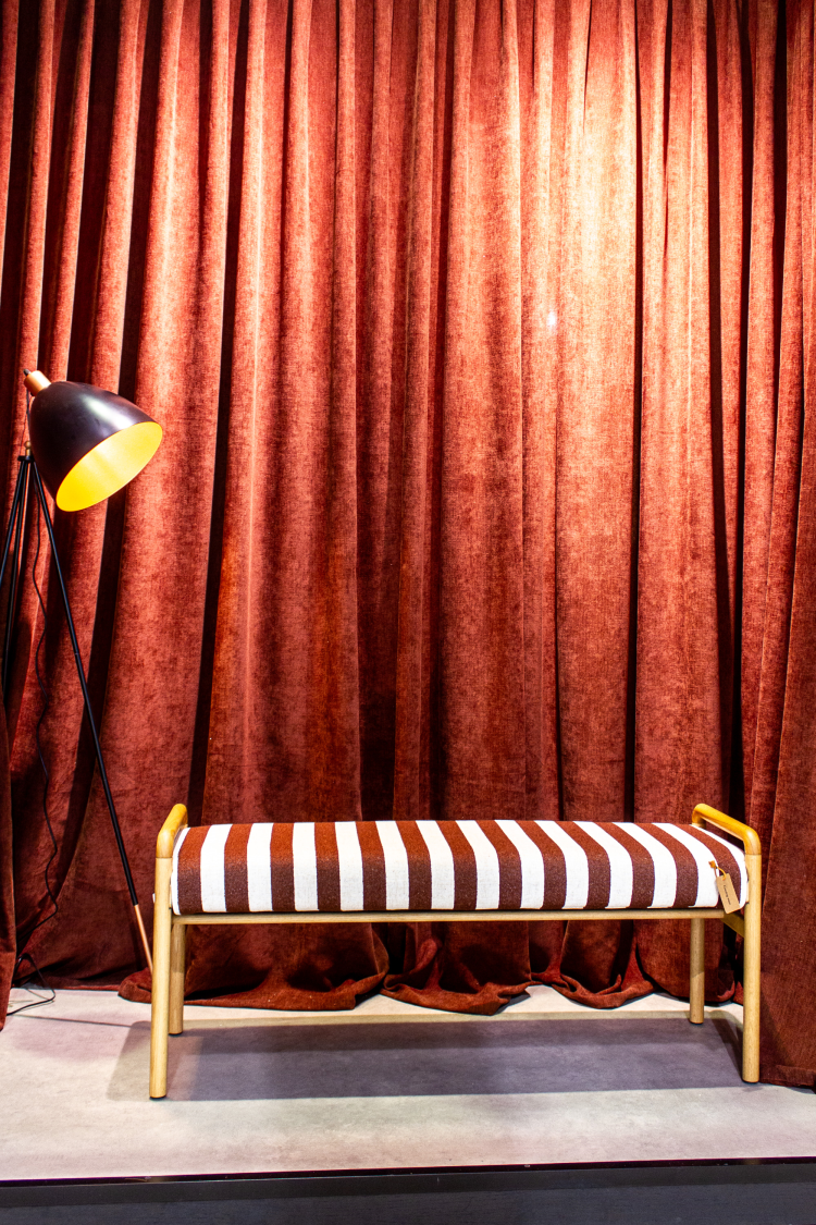 rødt gardin med liten benk foran. med rødt og hvitstripete tekstil