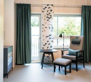 Synlig yttervegg i massivt tre gir beboerrommene en lun atmosfære og er et taktilt innslag sammen med rikelig bruk av gardiner, sengeteppe og polstrede møbler.<br />Foto: Espen Grønli