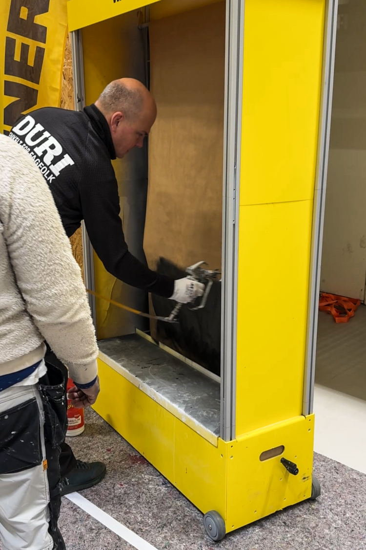 mann demonstrere maling med malesprøyte i en gul bås