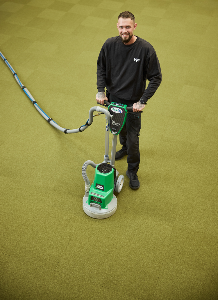 mann renser et grønt teppegulv med tepperensemaskin
