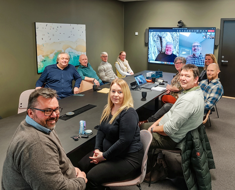 gruppe med menn og kvinner ved møtebord og to deltakere på TV-skjerm, fra Teams