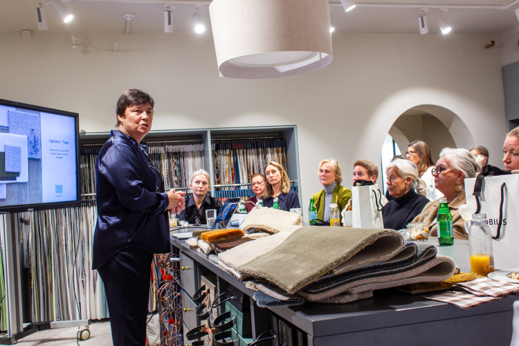 dame med mørkt kort hår holder foredrag for et sittende publikum i et showrom for interiørvarer