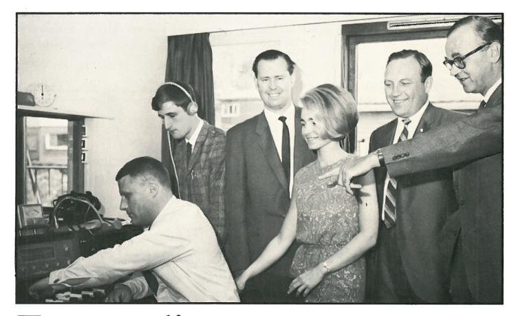 gammelt sorthvitt foto med menn og kvinner foran en radio