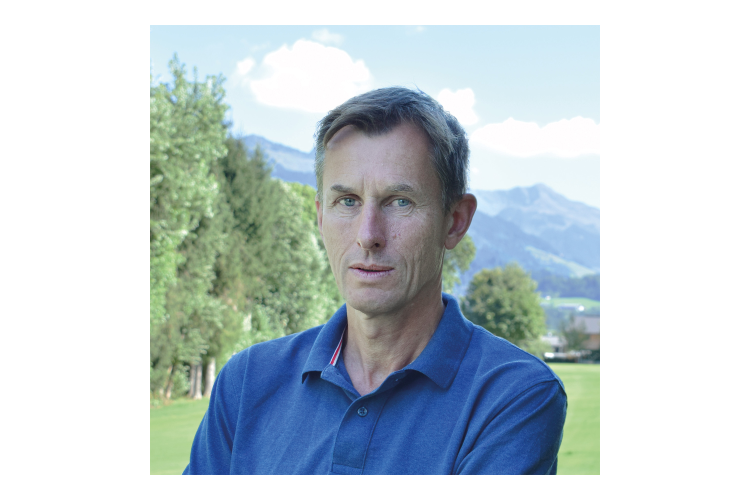 mann i blå skjorte mot naturbakgrunn med gress, trær og fjell