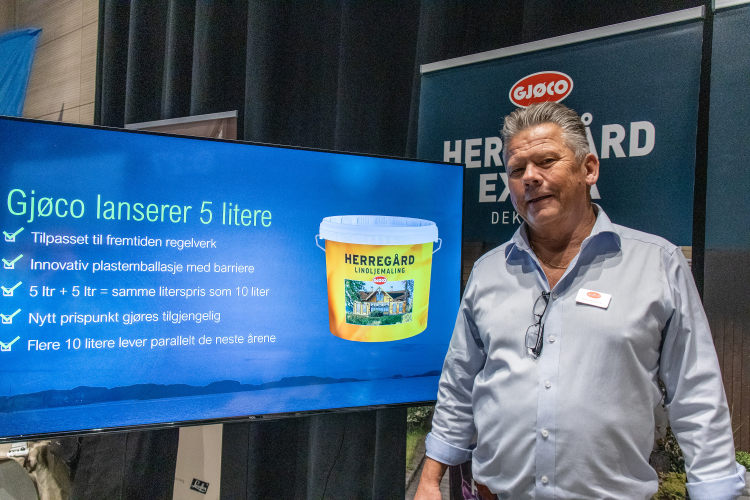 mann i blå skjorte foran tv-skjer med Gjøco