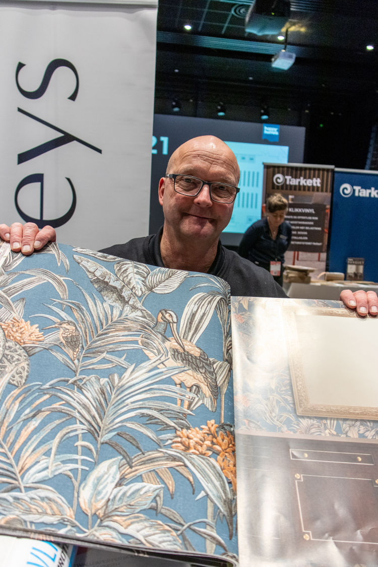 mann holder frem en tapetbok med blomstrete tapet 