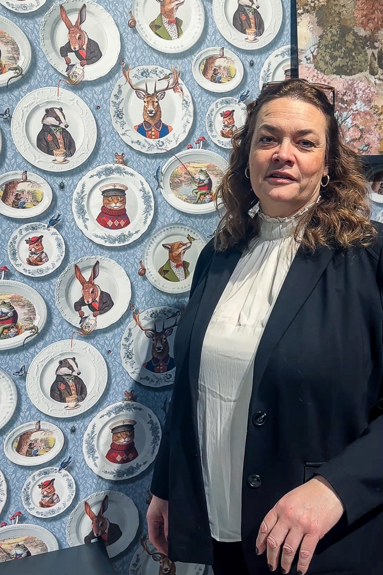 dame foran vegg med tapet med tallerkener med dyreportretter 