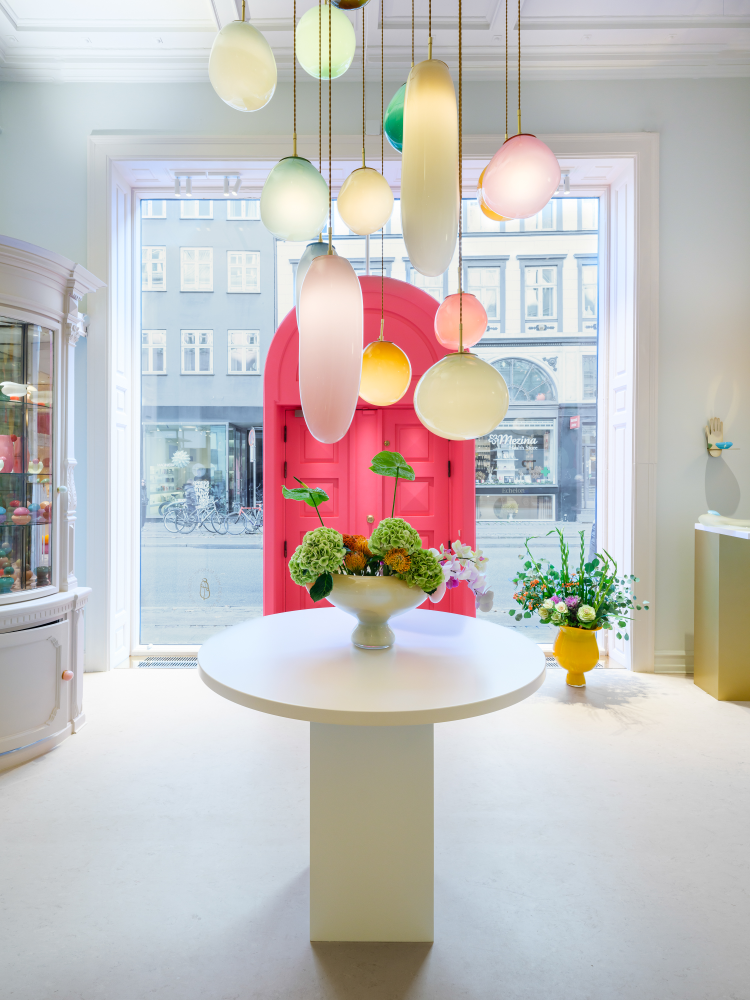 Butikkinteriør sett innenfra og ut mot vinduene. Fargerik glasskunst i butikken og en rosa dør. 