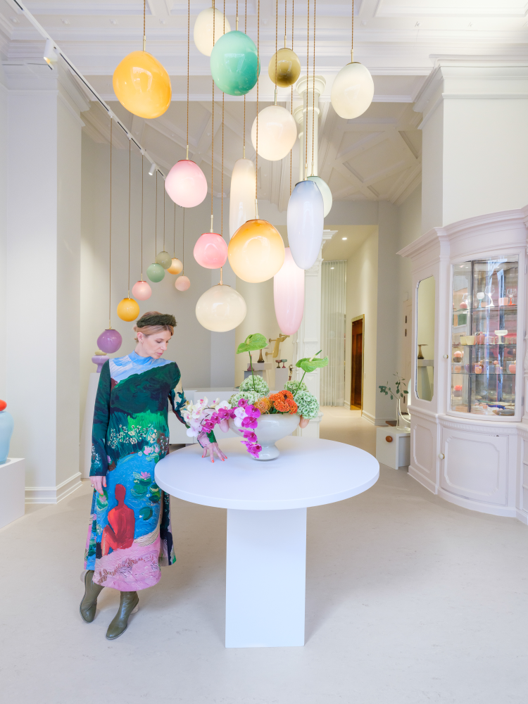 dame ved bord med glasskunst i en butikk med et knippe pendellamper hengende fra taket 