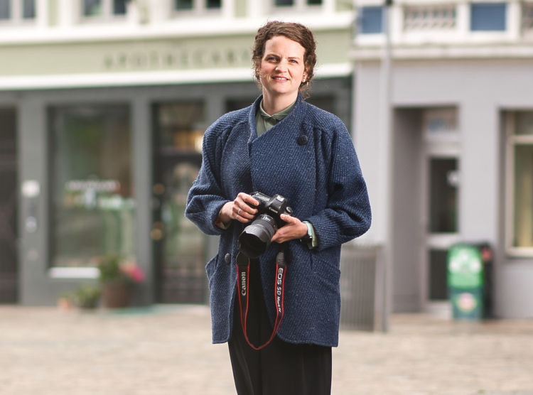dame i blå jakke i bymiljø med fotoapparat i hånden