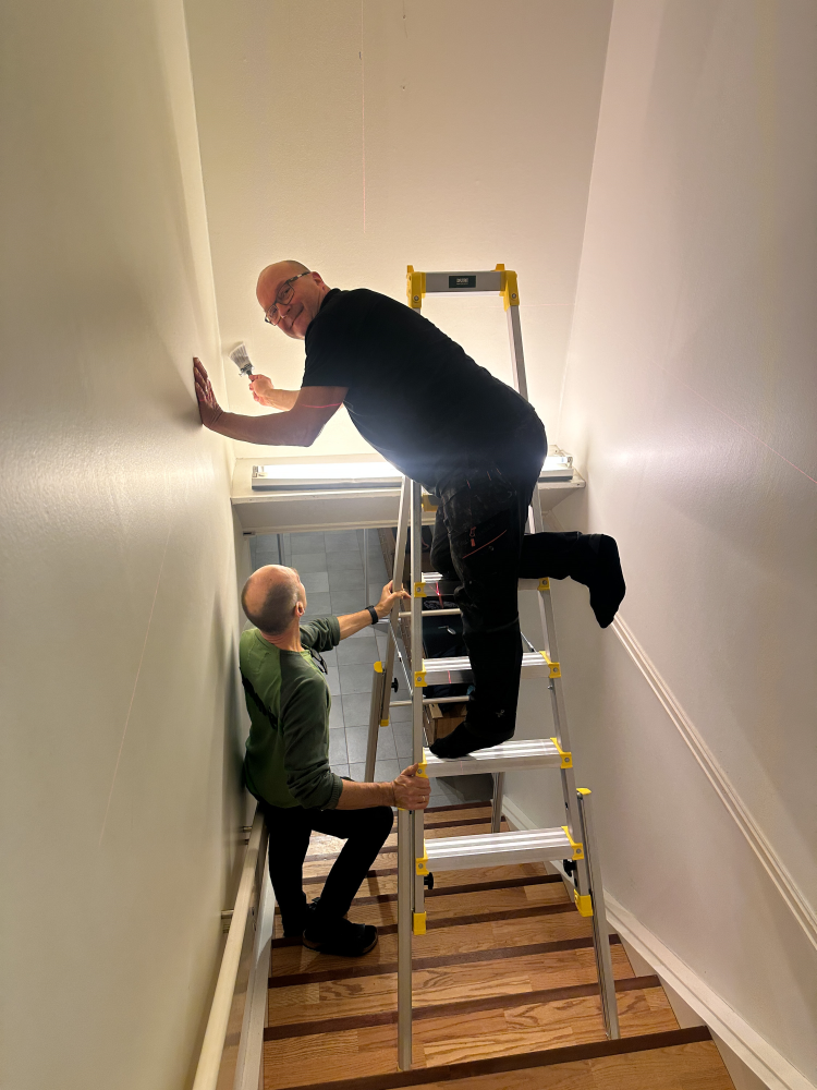 mann på stige i trapp setter opp tapet 