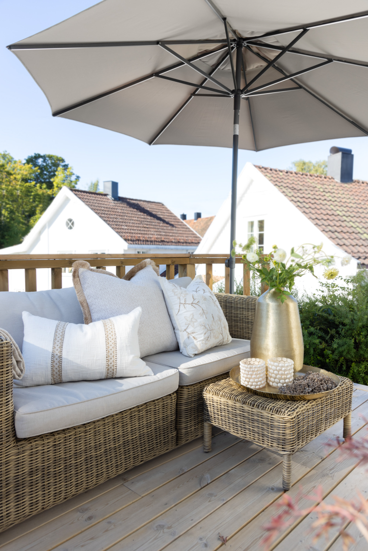 terrasse med sofa med hvite puter og en parasoll