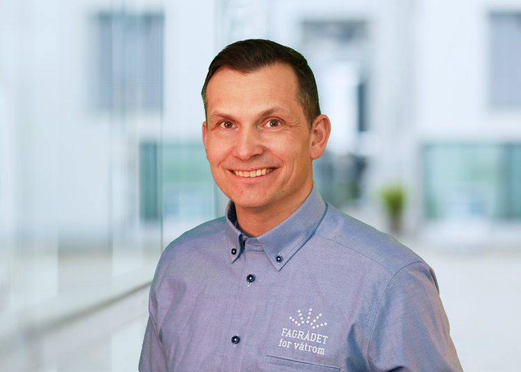 smilende mann i blå skjorte mot lys bakgrunn