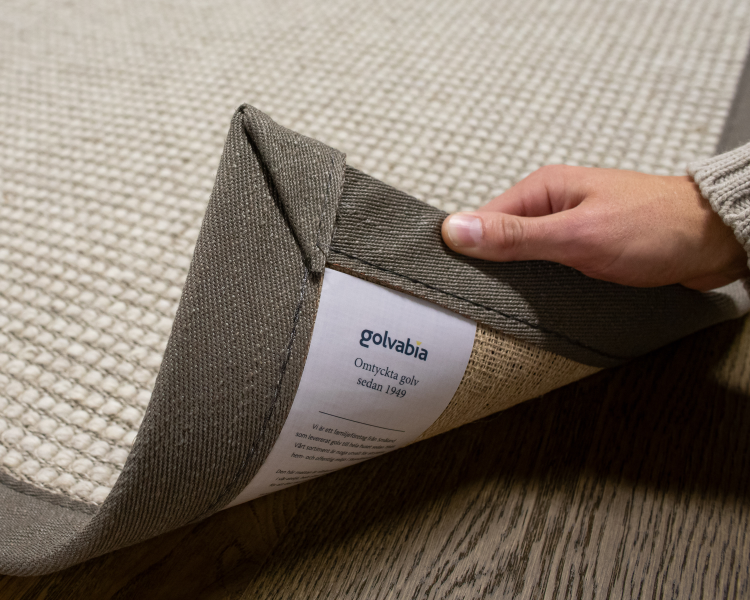 løfter på hjørnet av et avpasset teppe med bredt kantbånd