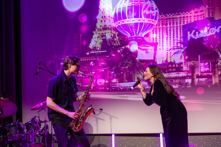 Mann med saksofon og dame med mikrofon spiller musikk og synger på en scene.