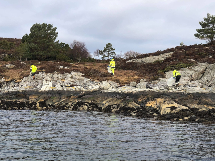 steinstrand med tre personer i gule klær