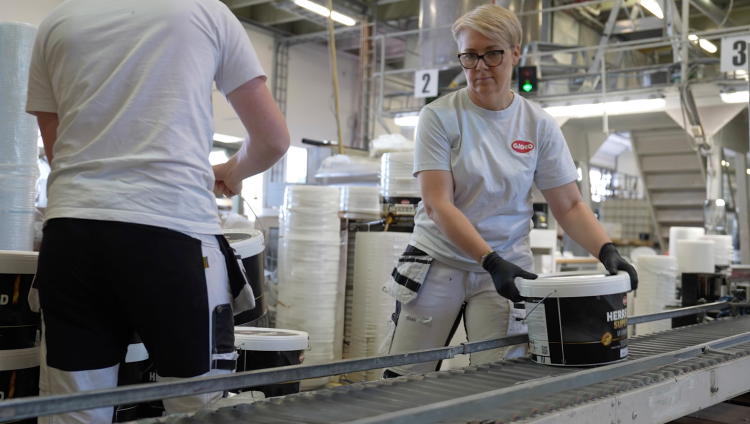 Person jobber på fabrikken til Gjøco, malingspann på bånd.