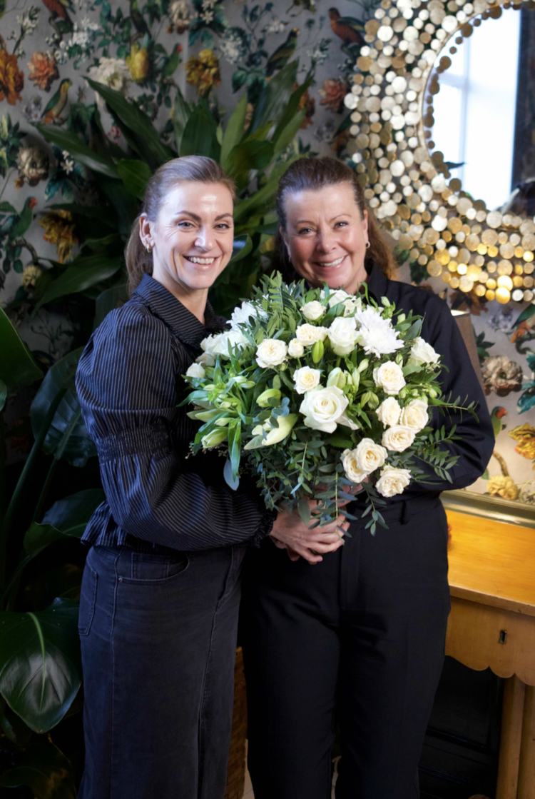 to damer med blomsterbukett foran tapetsert vegg