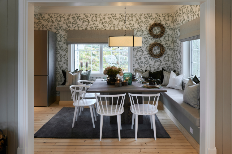 spiseplass i hytte kvadratisk bord, med benker på to sider og stoler på to. Tapet med grønne grener med barnåler på veggen