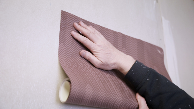 tett på to hender som holder opp et tapet mot veggen 